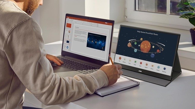 A person using a laptop and a MNN Portable 15.6" FHD Monitor together, while taking notes