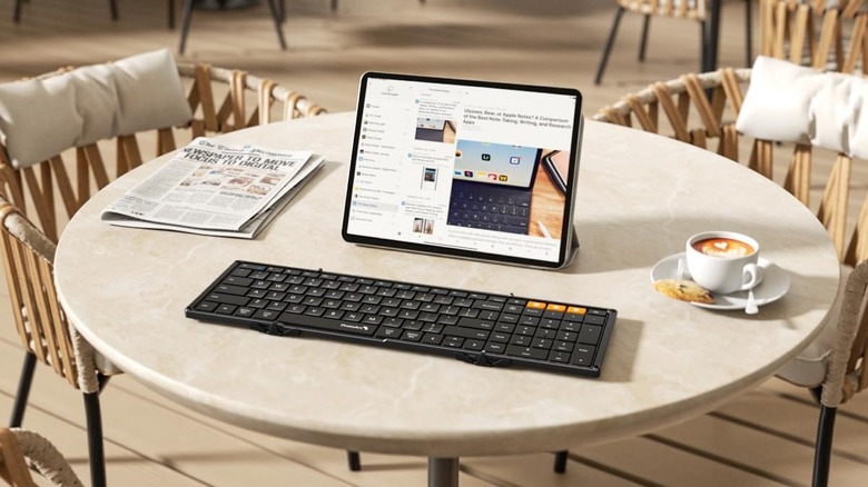 A round table with a newspaper, a cup of coffee, a tablet, and the ProtoArc XK01 Foldable Keyboard