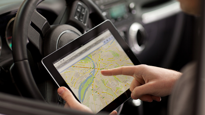 An individual using Google Maps navigation on iPad while in car
