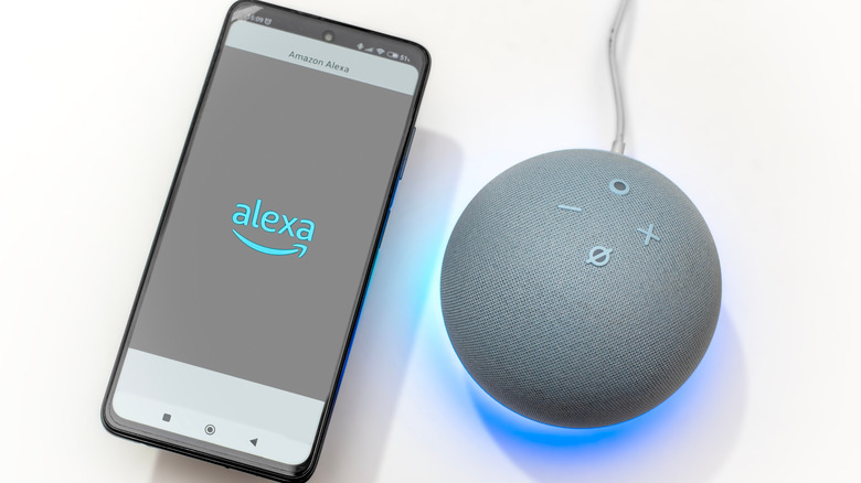 A phone with the Alexa logo next to an Echo Dot speaker on a white surface