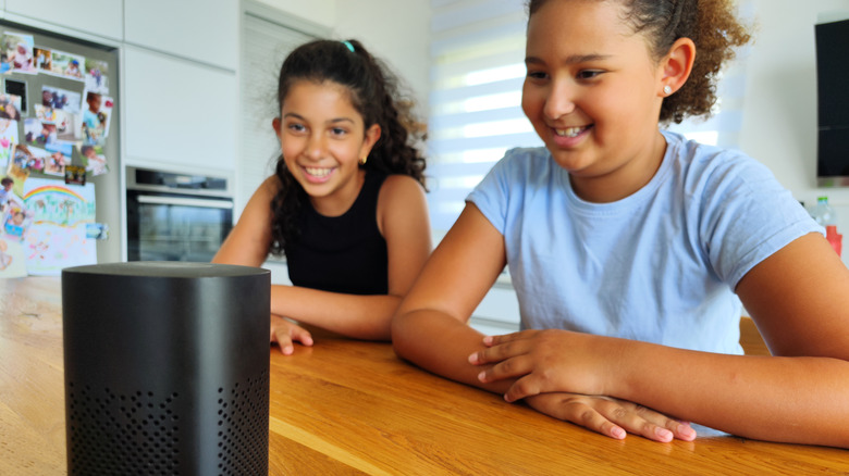 Two kids looking at a speaker placed on a wooden table with smiles on their faces