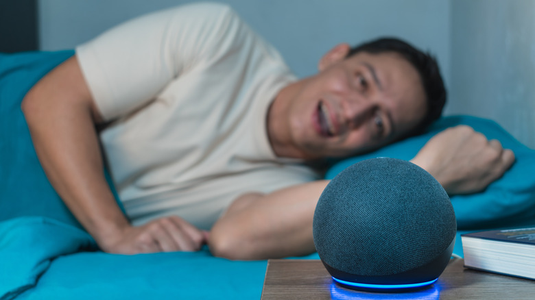 A smiling person lying in a bed with an Echo Dot on the bedside table