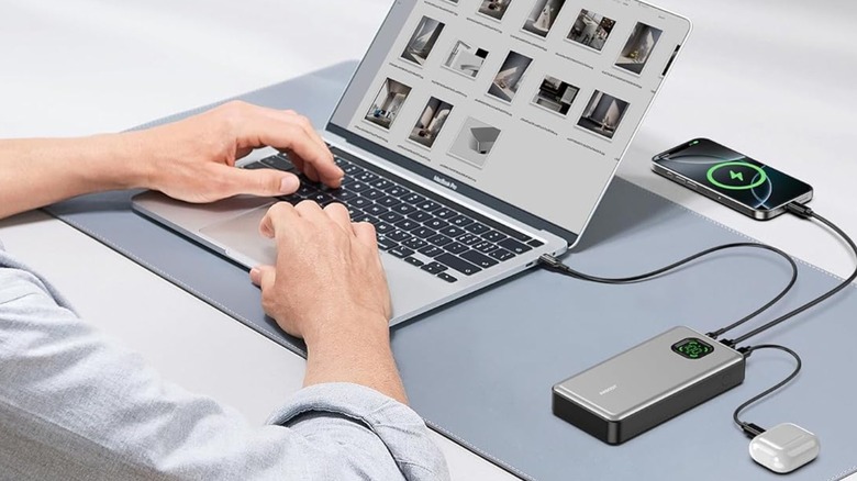 Person using power bank to charge laptop phone and earbuds