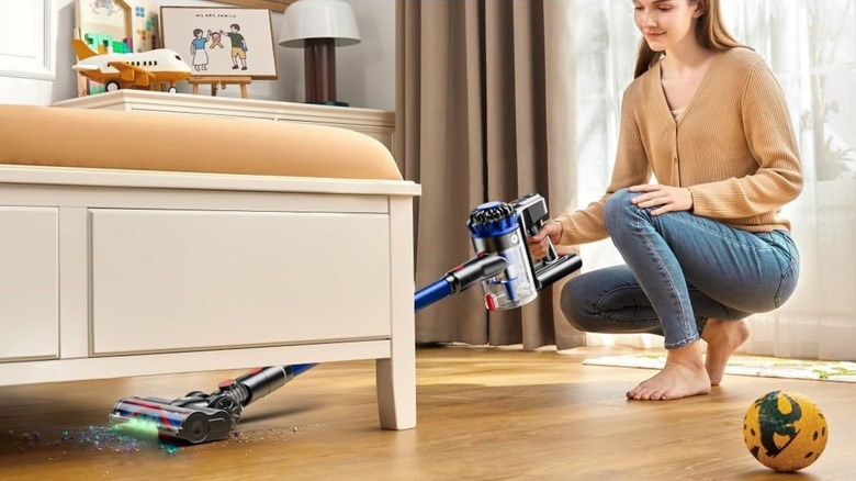 Woman using cordless vacuum cleaner to clean living room