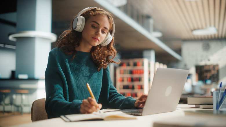A person wearing headphones while working on a laptop in a library.
