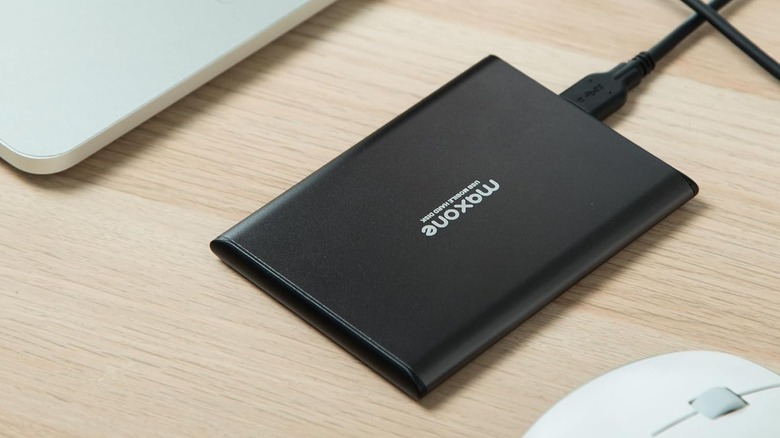 The Maxone 2519 external hard drive on a wooden desk, in between a laptop and a mouse.