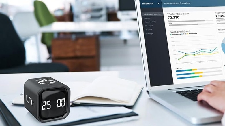 The OORAII F4 rotating timer on a desk, beside a person working on a laptop.