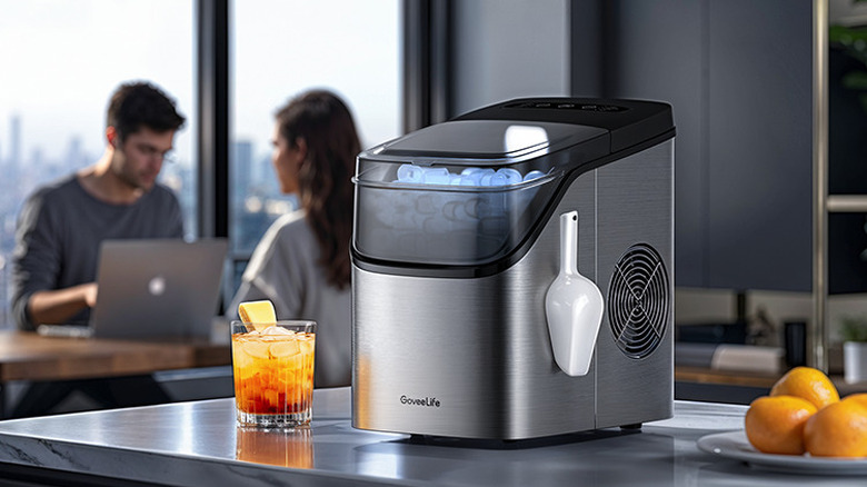 The GoveeLife H717D smart ice maker on a kitchen countertop with two people sitting at a table in the background.