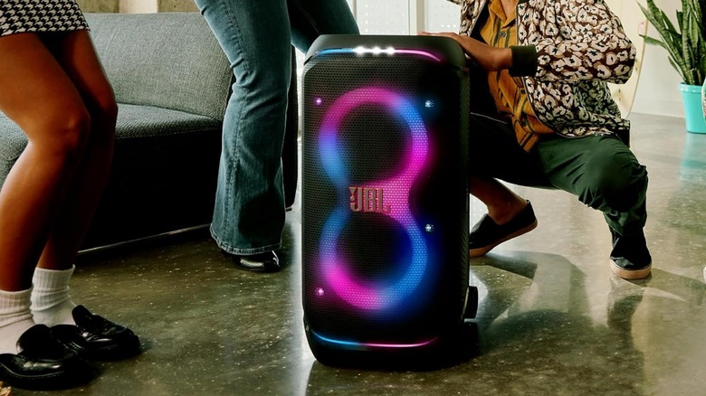 The JBL PartyBox Stage 320 portable speaker on the floor with people dancing around it.