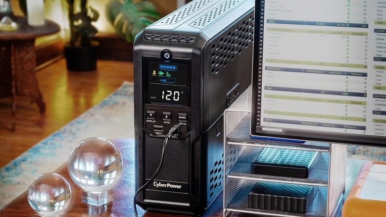 The CyberPower CP1500AVRLCD3 UPS on a desk, beside a monitor.