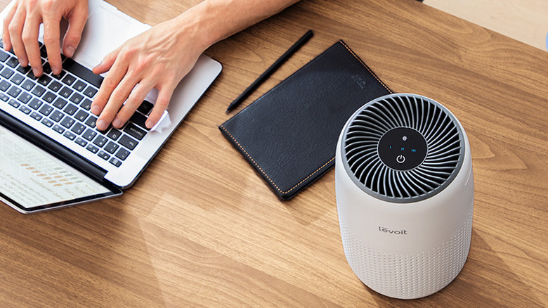 The Levoit Core Mini air purifier beside a laptop and notebook.