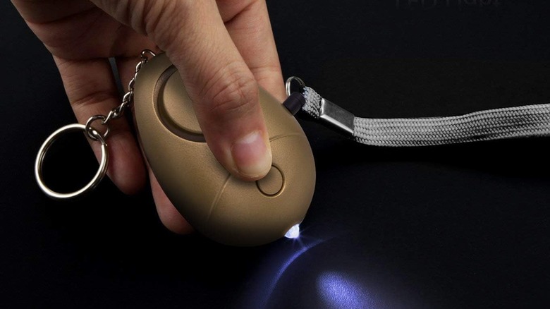 A hand operating the flashlight function of the Kosin XCT-014 personal safety alarm.