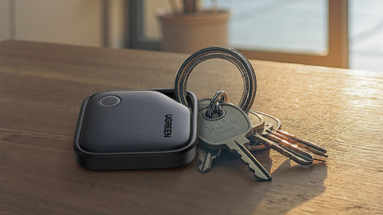 The UGREEN FineTrack tracker tag attached to a keychain on a wooden surface.
