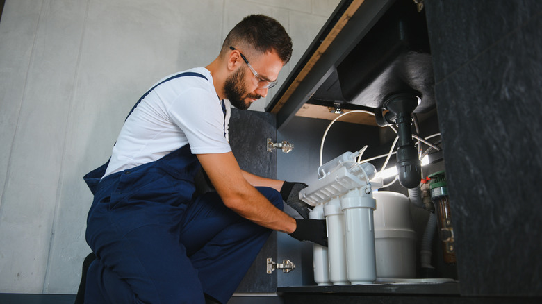 A man replacing a water filter under a sink