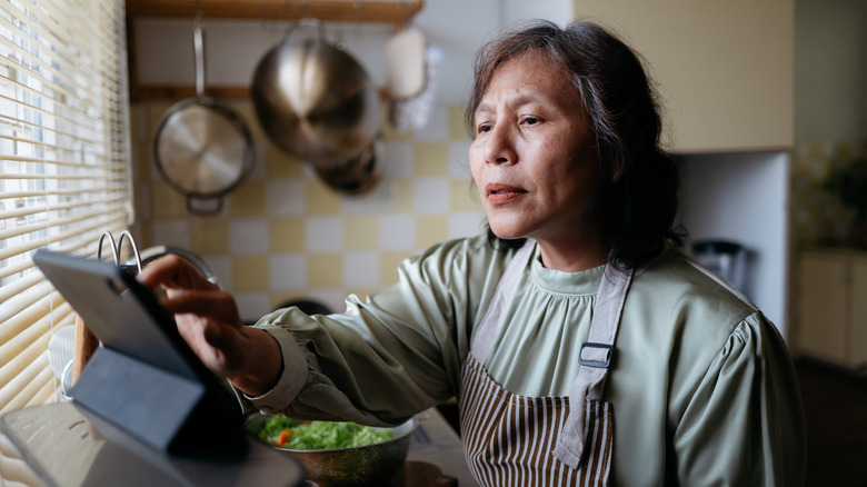 A woman touching a tablet screen at a kitchen countertop