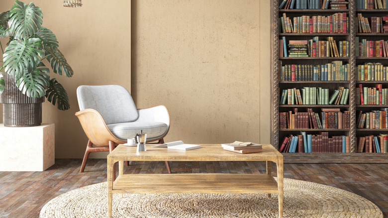 Cozy reading nook with a modern armchair, wooden coffee table, large houseplant, and floor-to-ceiling bookshelves filled with books.