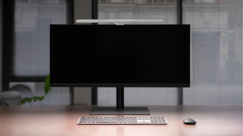 Ultrawide monitor on a minimalist desk with a monitor-mounted light bar providing even illumination across the workspace, alongside a keyboard and mouse.