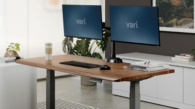 The Vari Comfort Edge Standing Desk with two monitors and accessories in an office setting.