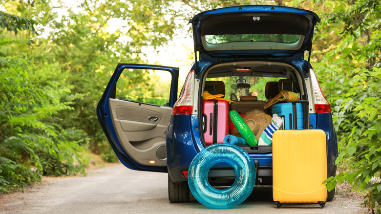 A fully laden car boot with luggage for a holiday sits at the side of a rural road