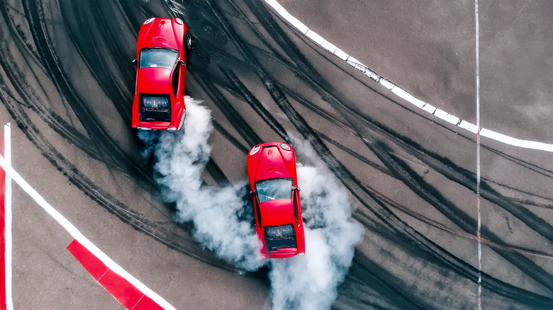 Top down view of two cars racing on a track with tires making smoke