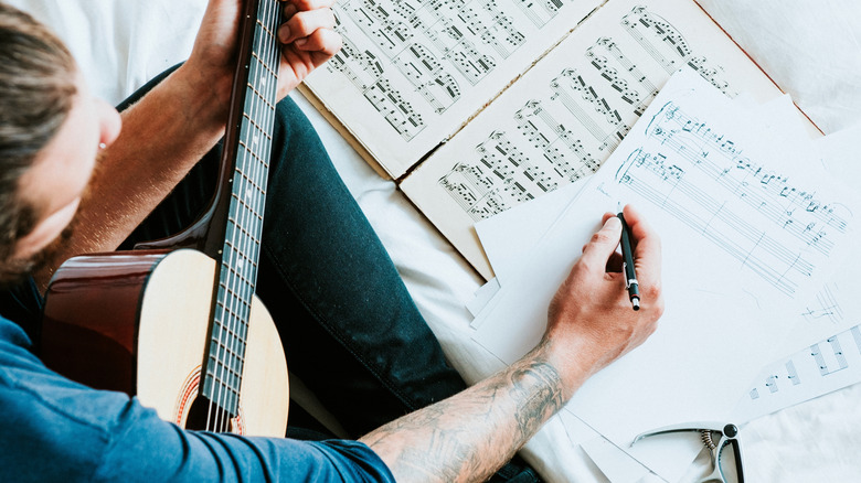 Man writing down lyrics as he holds a guitar