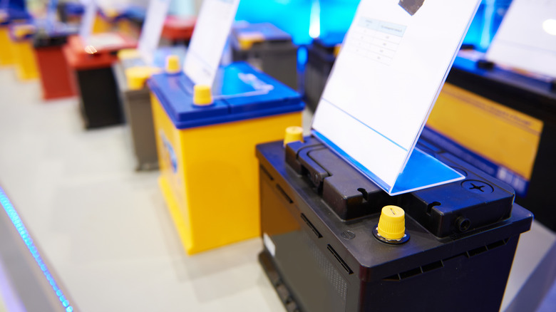 Several different colored car batteries displayed on a shelf in a store.