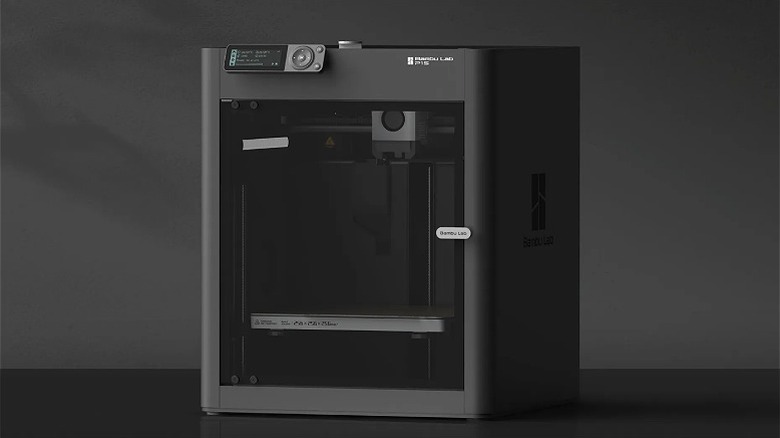 3D printer placed on a black surface against a grey background.