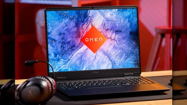 Omen logo on a laptop screen with headphones placed beside it.