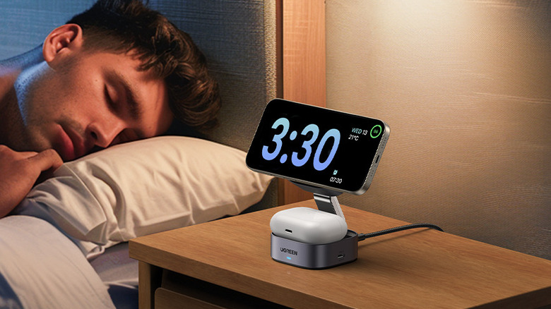 The Ugreen MagFlow 2-in-1 charging station on a bedside table charging a phone and wireless earbuds.