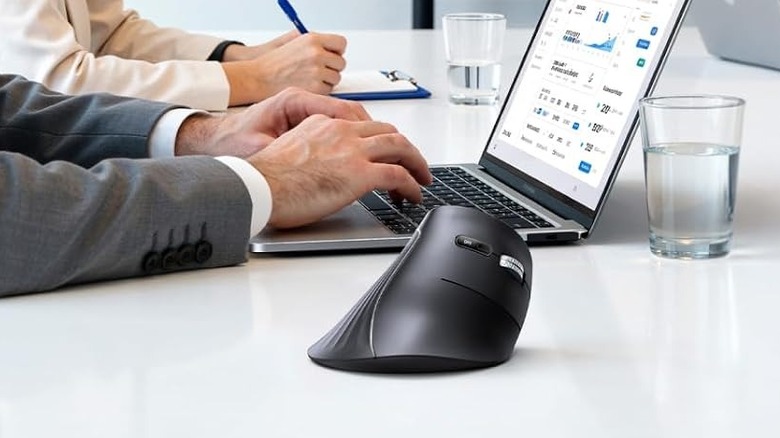 The Ugreen vertical wireless ergonomic mouse on a white table beside a laptop.