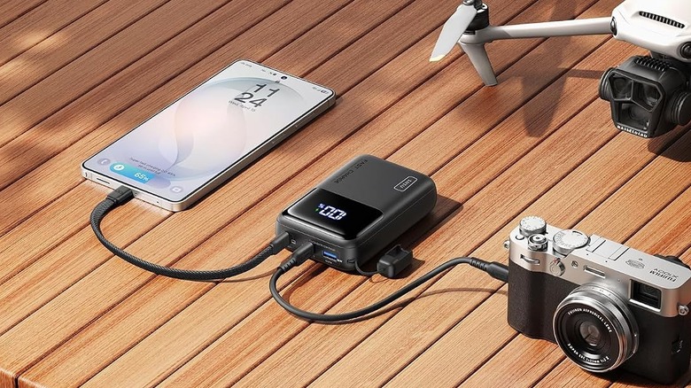 The INIU P62 power bank on a wooden deck, charging a phone and a camera.