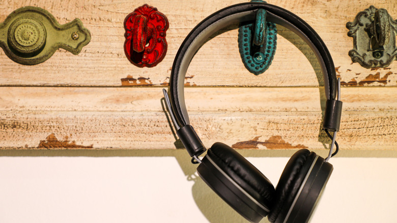 Headphones hanging on a hook mounted to a wooden board.