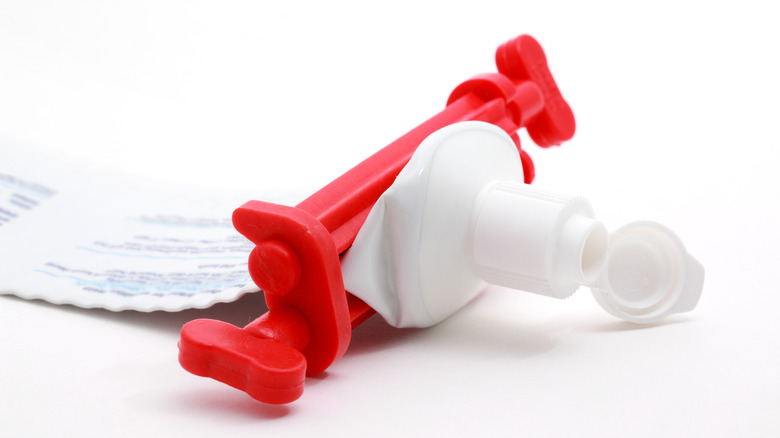 A red plastic toothpaste squeezer attached to a toothpaste tube.