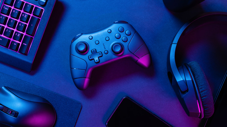 Flat shot of a desktop featuring a game controller, headset, keyboard, and mouse with blue and purple lighting