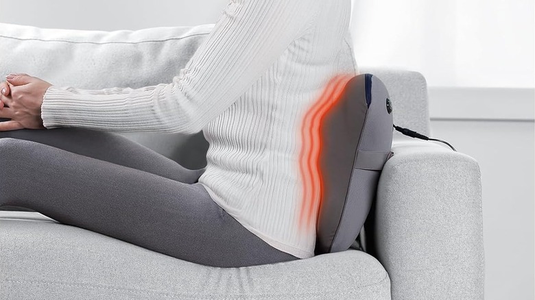 A person using the Bob and Brad EZBack massager on their back while sitting on a sofa.