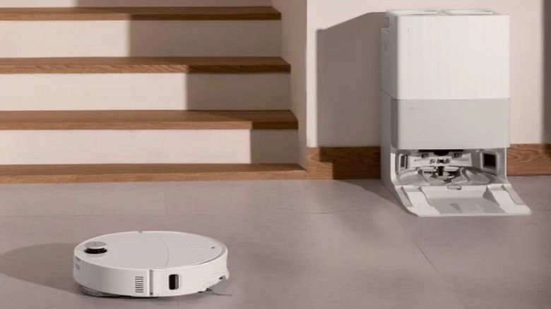 The Revo Ultra robot with on a floor in front of steps with its charging station against the nearby wall