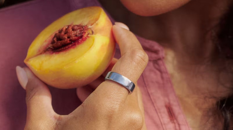 A person wearing the Oura Ring 5 smart ring while holding a fruit.