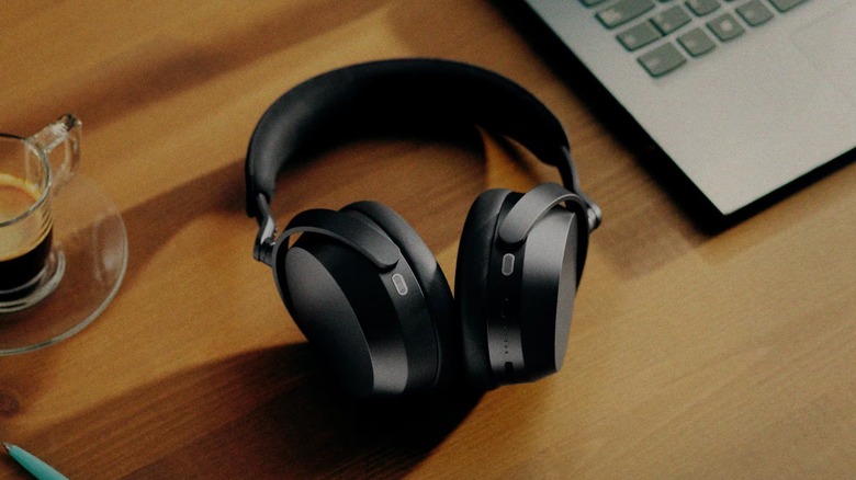 THe Sennheiser Momentum 5 Wireless headphones on a table, between a coffee mug and a laptop.