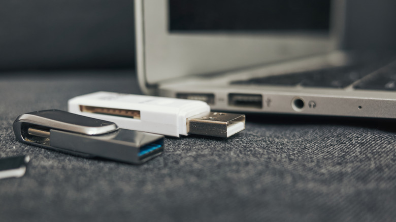 A laptop in the background showing its USB-A ports with several USB-A flash drives in the  foreground.