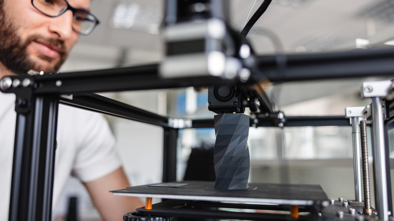 A man watches as his black vase is 3D printed