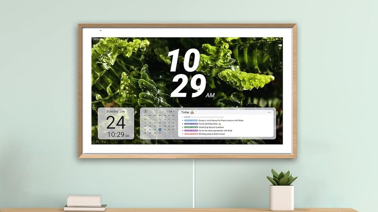 The Apologsign digital calendar on a wall with a potted plant and books nearby