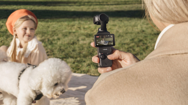 A person using the DJI Osmo Pocket 3 gimbal camera to take a video of a girl and a dog.
