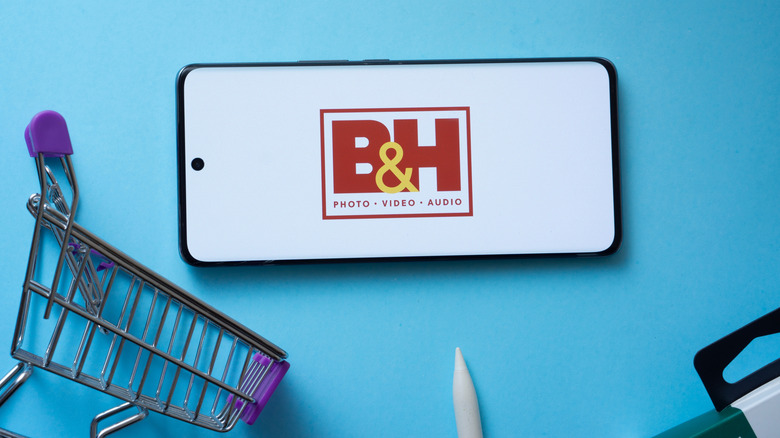 A smartphone with the B&H Photo Video logo on the screen, with a mini shopping cart beside it.