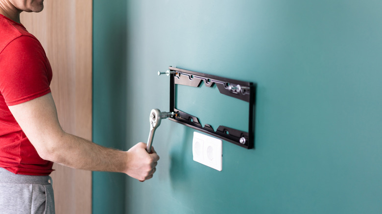 A person tightens the bolts on a TV mounting plate.