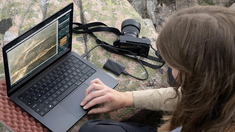 A woman using a laptop outdoors that has a Samsung SSD plugged into the USB port
