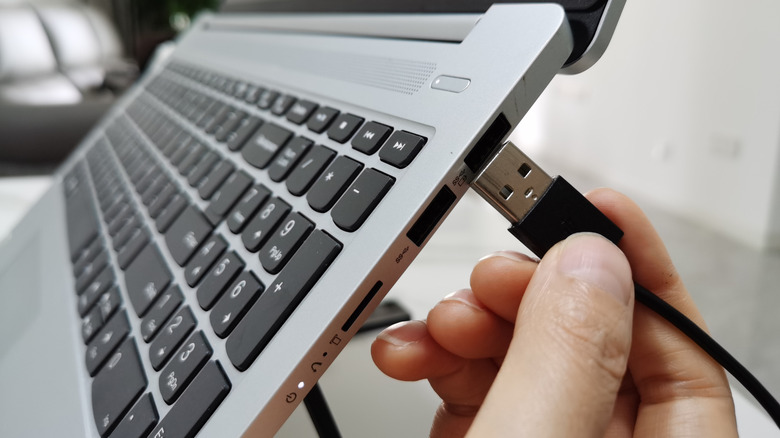Close up of hands plugging a USB-A cable into the USB-A port on a laptop