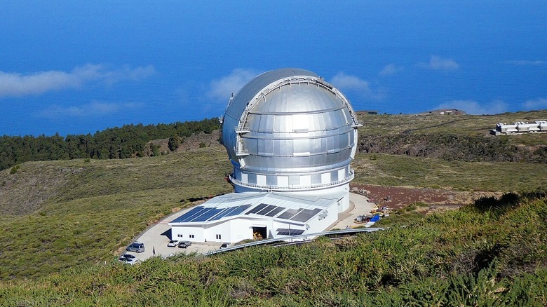 Photo of the Gran Telescopio Canarias above the clouds and surrounded by ample green grass