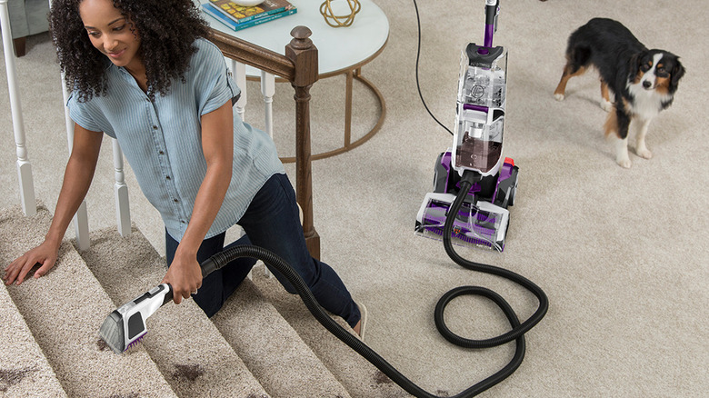 A woman using the Hoover SmartWash Pet Complete FH53000PC carpet cleaner to clean carpeted stairs.