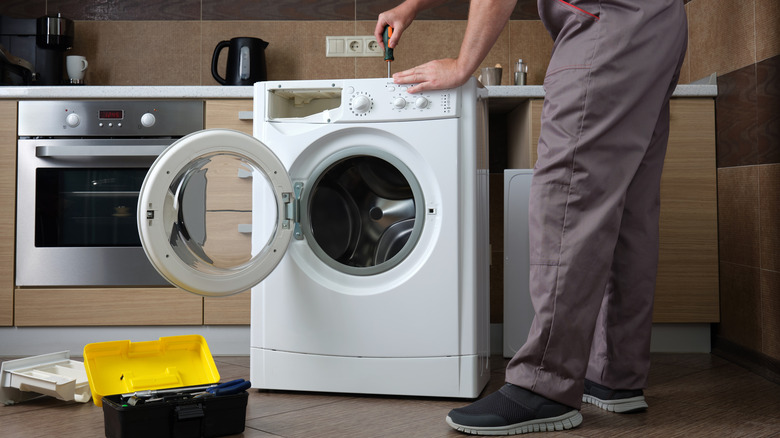 A repairman trying to fix a washing machine.