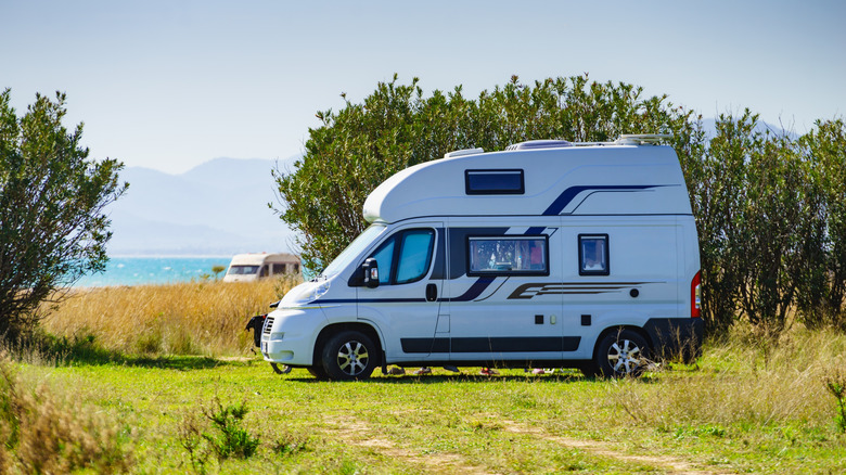A van RV parked in a sunny field with water in the distance